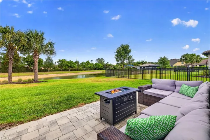 Paver patio featuring a fire pit table, direct lawn access, and a black wrought iron fence