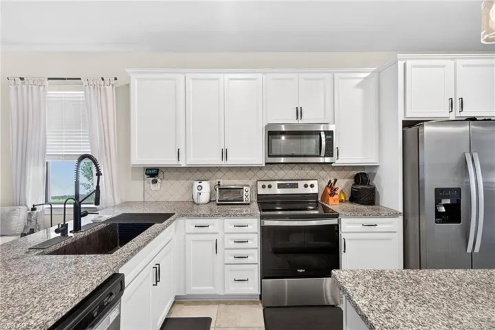 Kitchen featuring white shaker-style cabinetry with matte black hardware, granite countertops, stainless steel appliances, and a tiled backsplash