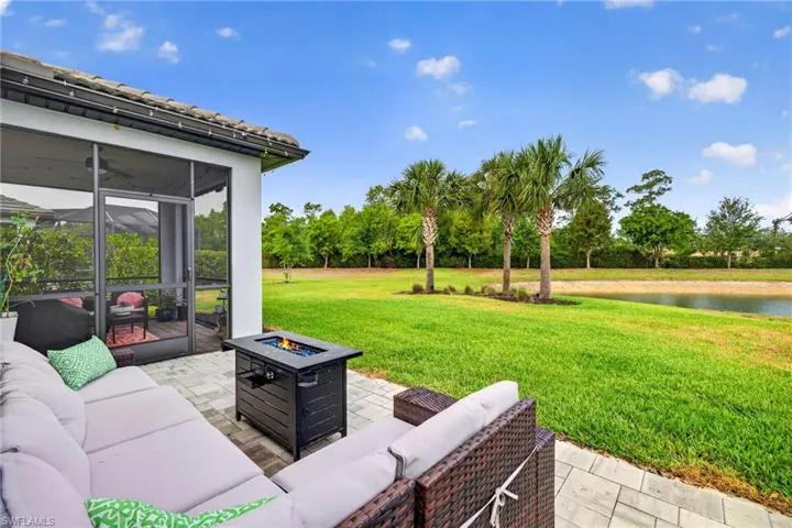 Screened lanai and paver patio with a fire pit overlooking a grassy area and pond