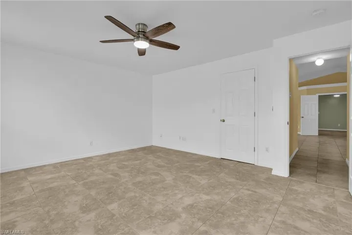 Spacious room featuring neutral tile flooring, a modern ceiling fan with integrated lighting, and a white paneled door
