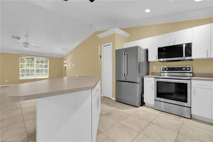 Kitchen island with light-toned countertop, stainless steel appliances, white cabinetry, and tile flooring