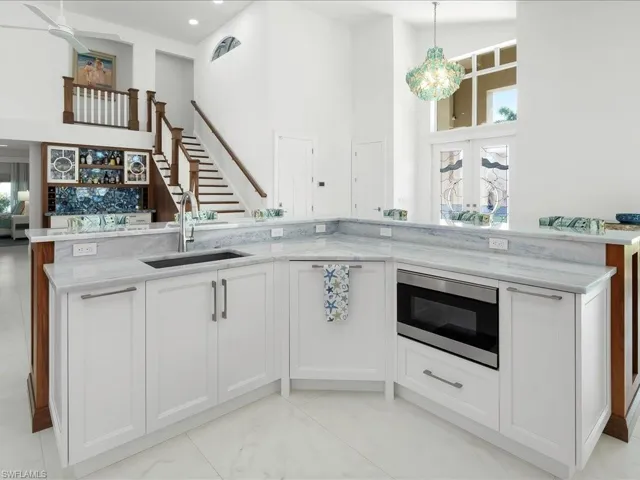 Kitchen featuring stainless steel microwave, light stone counters, a high ceiling, hanging light fixtures, and a sink