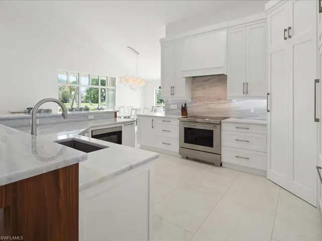 Kitchen with stainless steel electric range oven, light stone counters, custom exhaust hood, white cabinetry, and backsplash