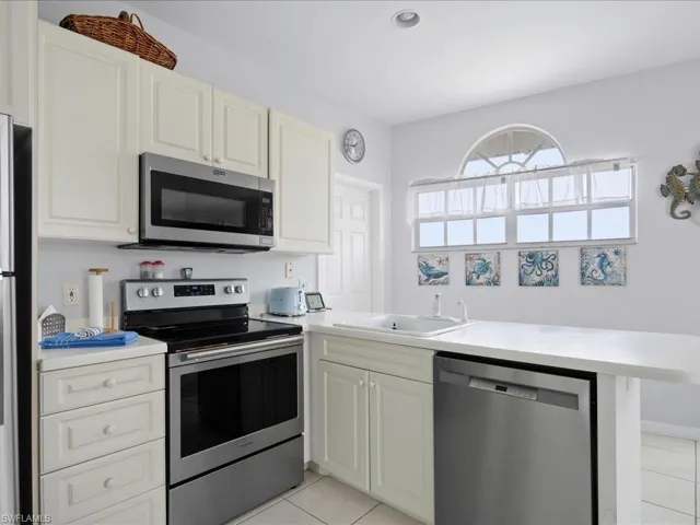Kitchen featuring light countertops, light tile patterned floors, a peninsula, stainless steel appliances, and a sink