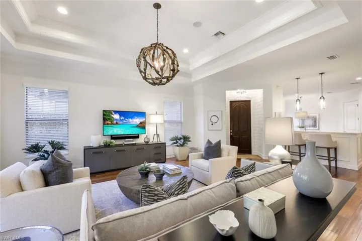 Living room with ornamental molding, a raised ceiling, light hardwood / wood-style flooring, and a notable chandelier