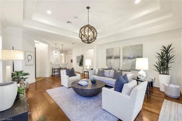 Living room with an inviting chandelier, a tray ceiling, and dark wood-type flooring