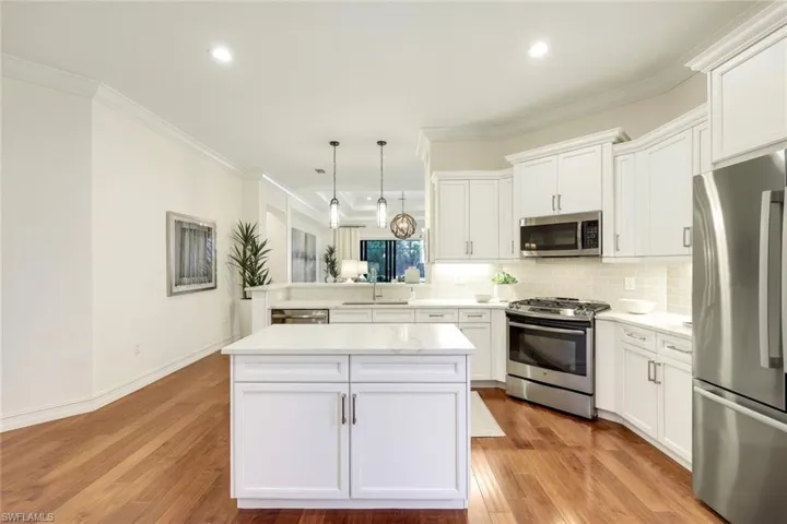 Kitchen featuring white cabinetry, appliances with stainless steel finishes, ornamental molding, kitchen peninsula, and pendant lighting