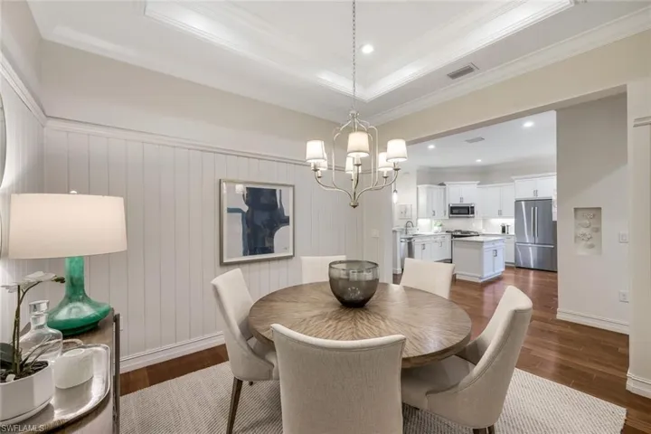 Dining room with an inviting chandelier, crown molding, dark wood-type flooring, and a raised ceiling