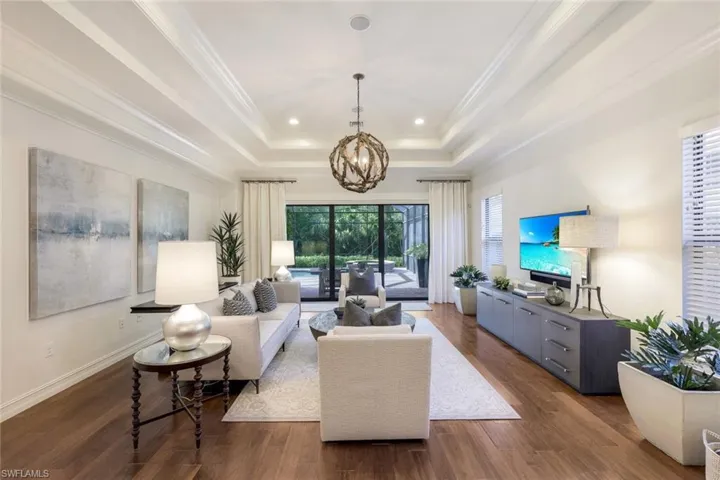 Living room featuring a raised ceiling, crown molding, a notable chandelier, and dark hardwood / wood-style flooring
