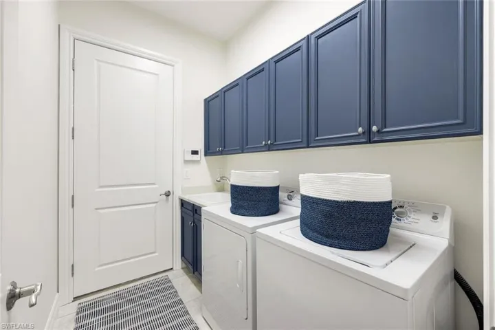 Laundry area with cabinets, light tile patterned floors, sink, and washing machine and clothes dryer