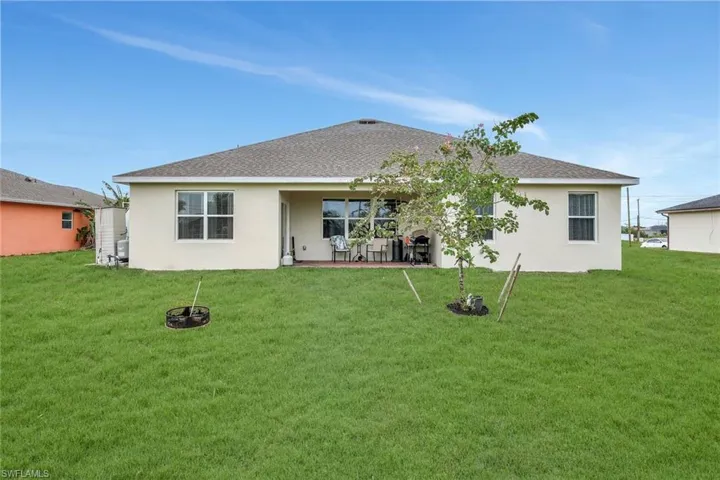 Rear view of house with roof with shingles, stucco siding, a yard, and a patio area