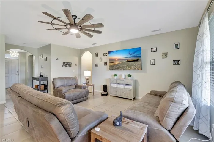 Living area featuring arched walkways, light tile patterned floors, baseboards, and a ceiling fan