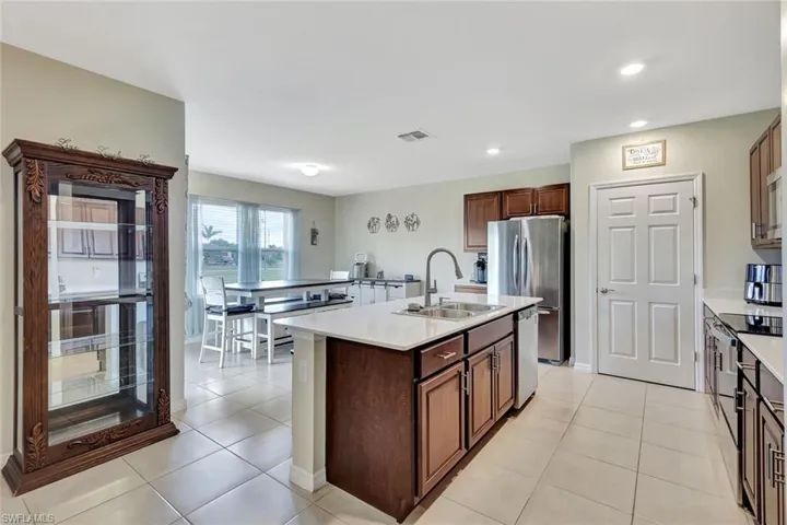 Kitchen with light countertops, a sink, appliances with stainless steel finishes, light tile patterned floors, and a kitchen island with sink