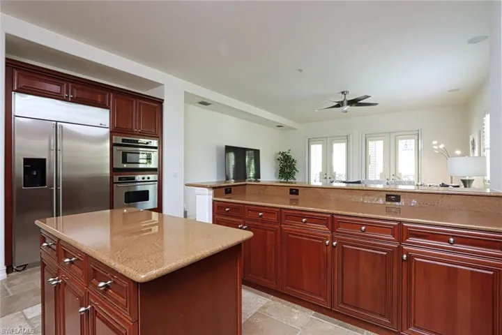 Kitchen with appliances with stainless steel finishes, dark brown cabinets, stone tile floors, a ceiling fan, and a center island