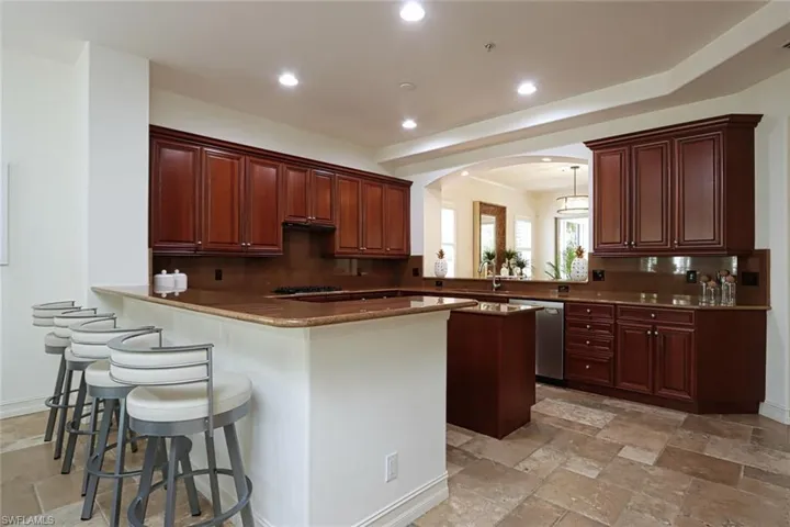 Kitchen with stainless steel dishwasher, arched walkways, a peninsula, stone tile floors, and recessed lighting