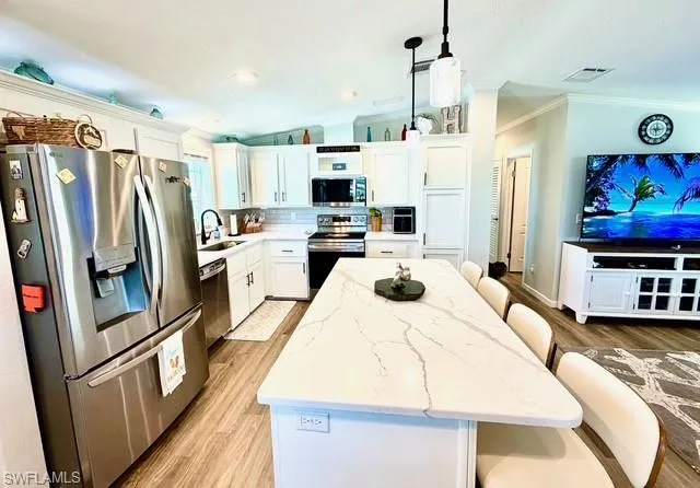 Kitchen with a breakfast bar, stainless steel appliances, white cabinets, a kitchen island, and ornamental molding