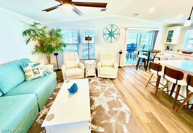 Living room featuring light wood finished floors, crown molding, a ceiling fan, and lofted ceiling