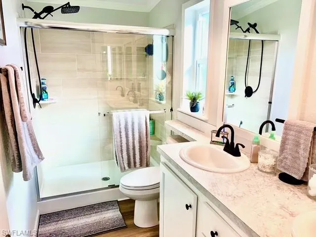 Full bathroom with double vanity, a shower stall, light wood-type flooring, and ornamental molding