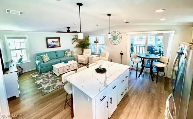 Kitchen featuring a breakfast bar, a center island, light stone countertops, stainless steel refrigerator, and light wood-type flooring