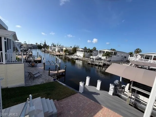 Dock featuring boat lift, a water view, a residential view, and a patio area