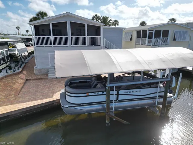 Dock area with boat lift, a water view, a sunroom, and a patio area