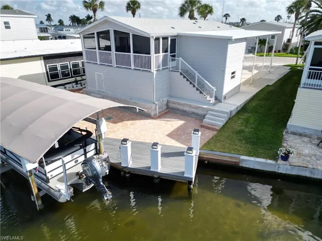 Back of property with boat lift, a patio area, a sunroom, and a water view