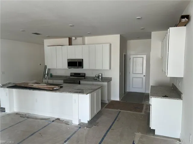 Kitchen with stone countertops, concrete floors, white cabinets, sink, and appliances with stainless steel finishes