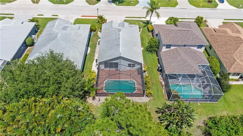 Screened-in swimming pool with an integrated spa, surrounded by a paved patio and green landscaping