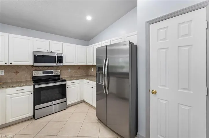 Kitchen featuring white cabinetry, granite countertops, tile backsplash, and stainless steel appliances