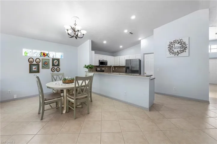 Open-concept kitchen and dining area featuring tile flooring, white cabinetry, and a peninsula with a stone-finish countertop