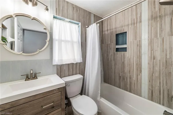 Bathroom featuring a tub/shower combination with a built-in niche, wood-look tile surround, and a coordinating vanity with an integrated sink