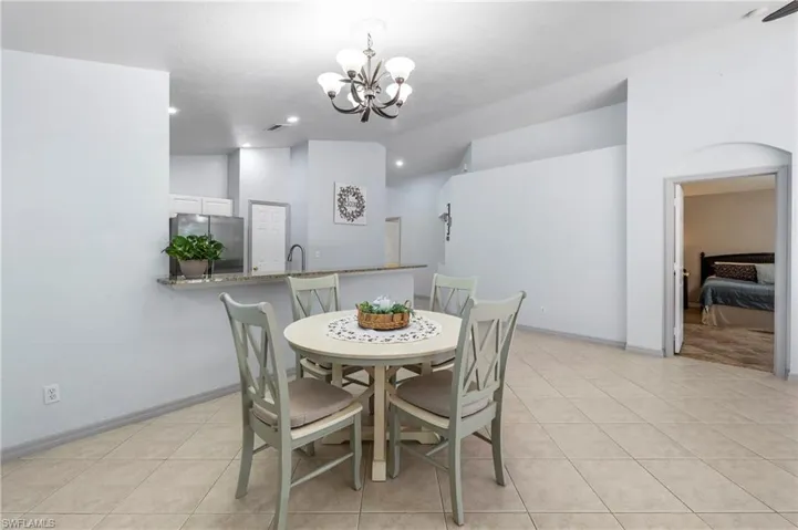 Open-concept dining area featuring a chandelier, tile flooring, an arched doorway, a breakfast bar with a stone countertop, and recessed lighting