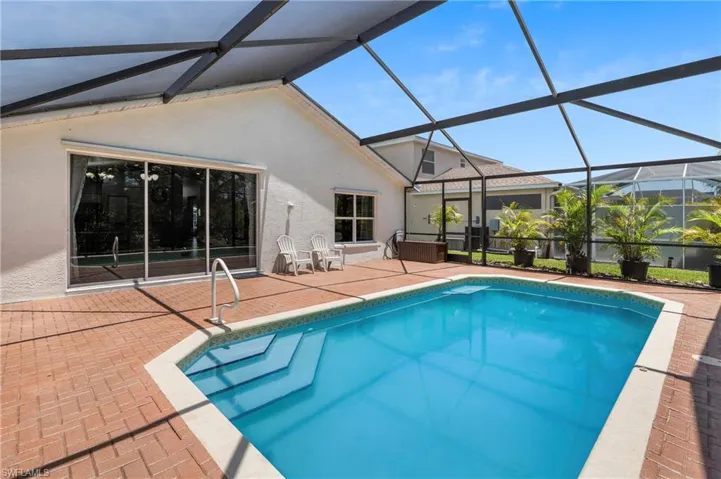 Screened-in pool area featuring a rectangular pool with integrated steps, brick paver decking, and a sliding glass door entry to the home
