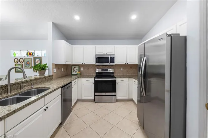 Kitchen featuring white cabinetry, stainless steel appliances, speckled stone countertops, and a double basin sink with a high-arc faucet
