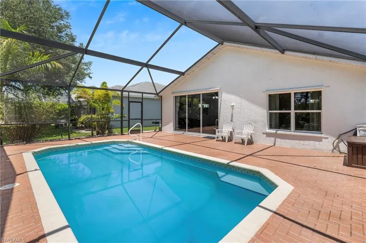 Screened-in pool area featuring a rectangular swimming pool with integrated steps, surrounded by brick-patterned hardscaping