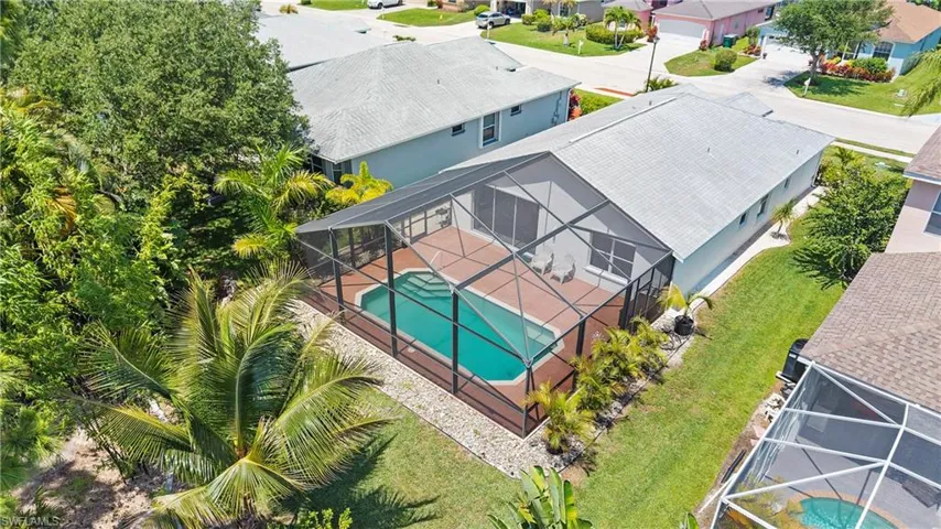Screened enclosure featuring a swimming pool with steps, a paved deck, and surrounding tropical foliage