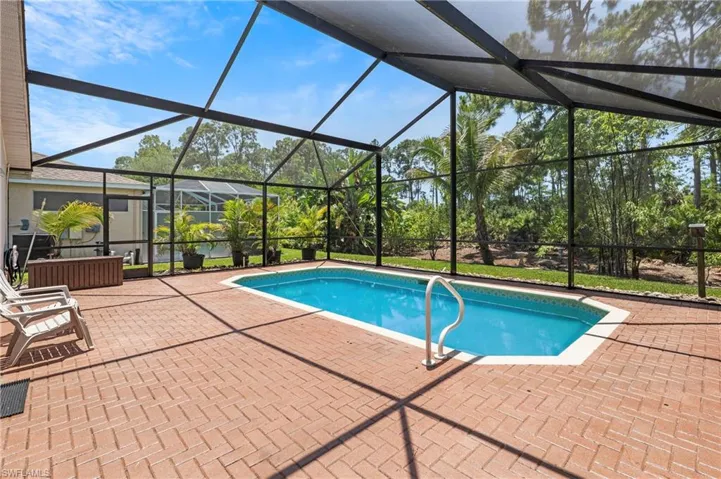 Screened-in outdoor living space featuring an in-ground swimming pool, brick paver patio, and lush surrounding landscaping