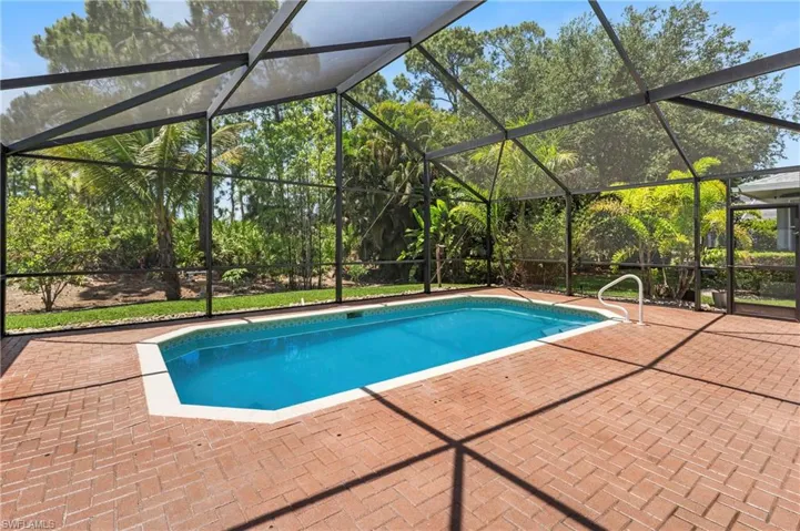 Screened enclosure featuring a geometric swimming pool with a white handrail, surrounded by a herringbone brick paver deck