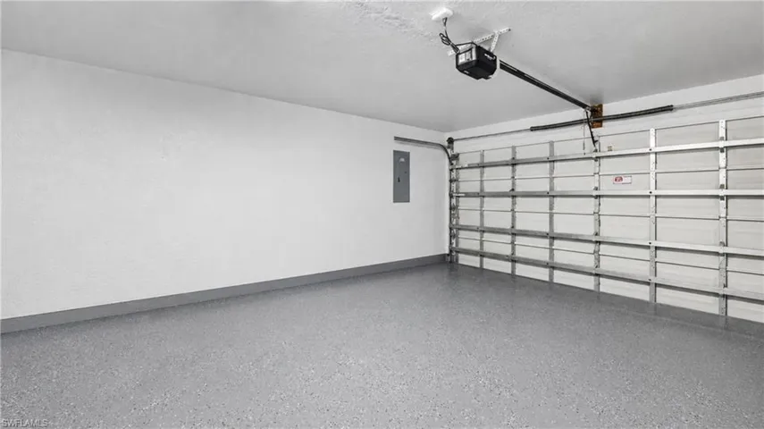Spacious garage featuring a durable epoxy floor finish, automatic garage door opener, white painted walls, and an electrical panel