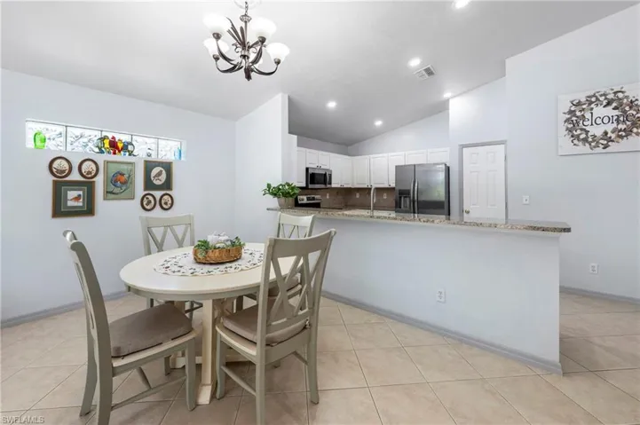 Kitchen and dining area featuring tile flooring, a breakfast bar with a granite-style countertop, white cabinetry, and recessed lighting