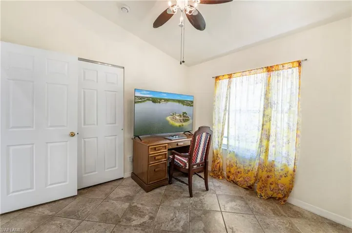 Vaulted ceiling room featuring large format tile flooring, a window with ample natural light, and a ceiling fan with integrated lighting