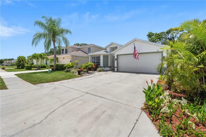 Single-story residence featuring a two-car garage with a paneled door, a concrete driveway, and a landscaped front yard with various plantings and a palm tree