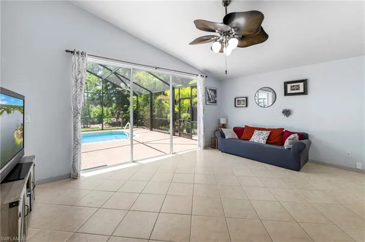 Living area featuring tile flooring, vaulted ceiling, and a ceiling fan with light fixture
