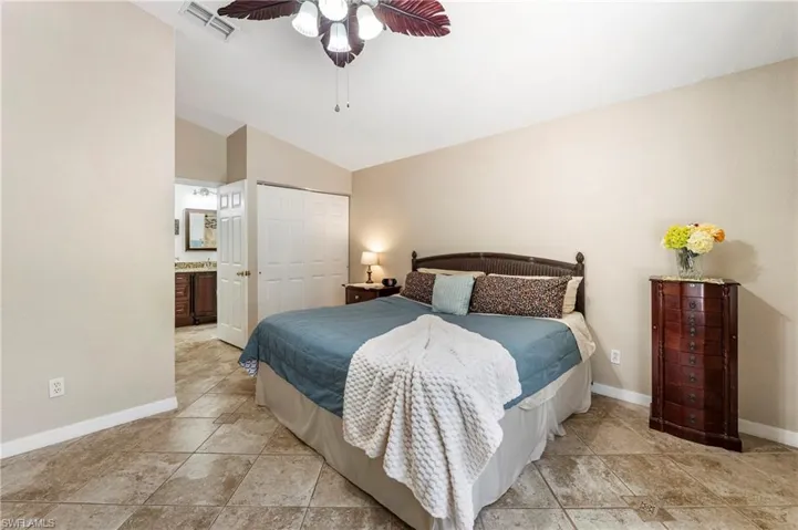 Bedroom featuring large format tile flooring, vaulted ceiling, and louvered closet doors