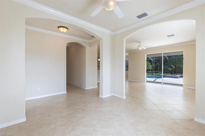 Spare room featuring crown molding, a ceiling fan, arched walkways, and light tile patterned flooring