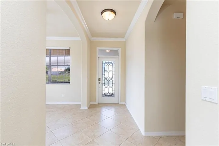 Entryway featuring arched walkways, crown molding, a textured wall, and light tile patterned floors