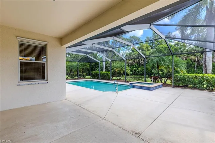 View of swimming pool with a patio, a sunroom, glass enclosure, a pool with connected hot tub, and view of scattered trees