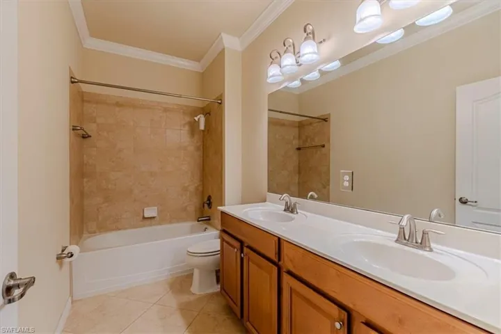 Full bathroom with washtub / shower combination, crown molding, double vanity, and light tile patterned flooring