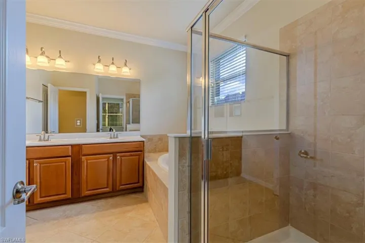 Full bath with a stall shower, a bath, double vanity, healthy amount of natural light, and ornamental molding