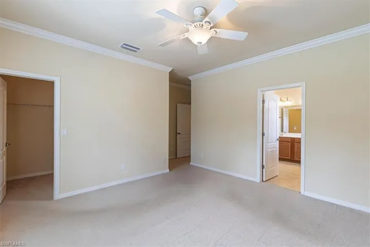 Unfurnished bedroom featuring crown molding, light carpet, a spacious closet, and a ceiling fan